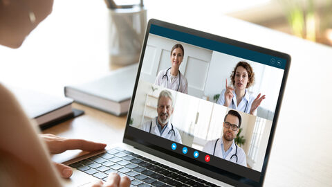 Person sitzt vor einem Laptop und hält eine Videokonferenz mit Ärzten