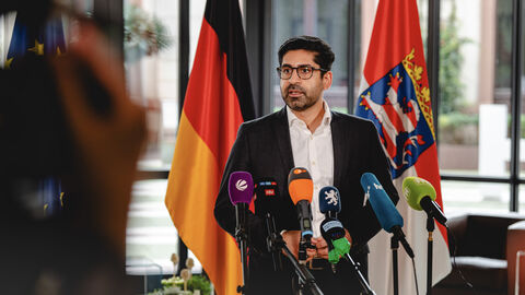 Wirtschaftsminister Mansoori steht vor Mikrofonen in einer Interviewsituation.